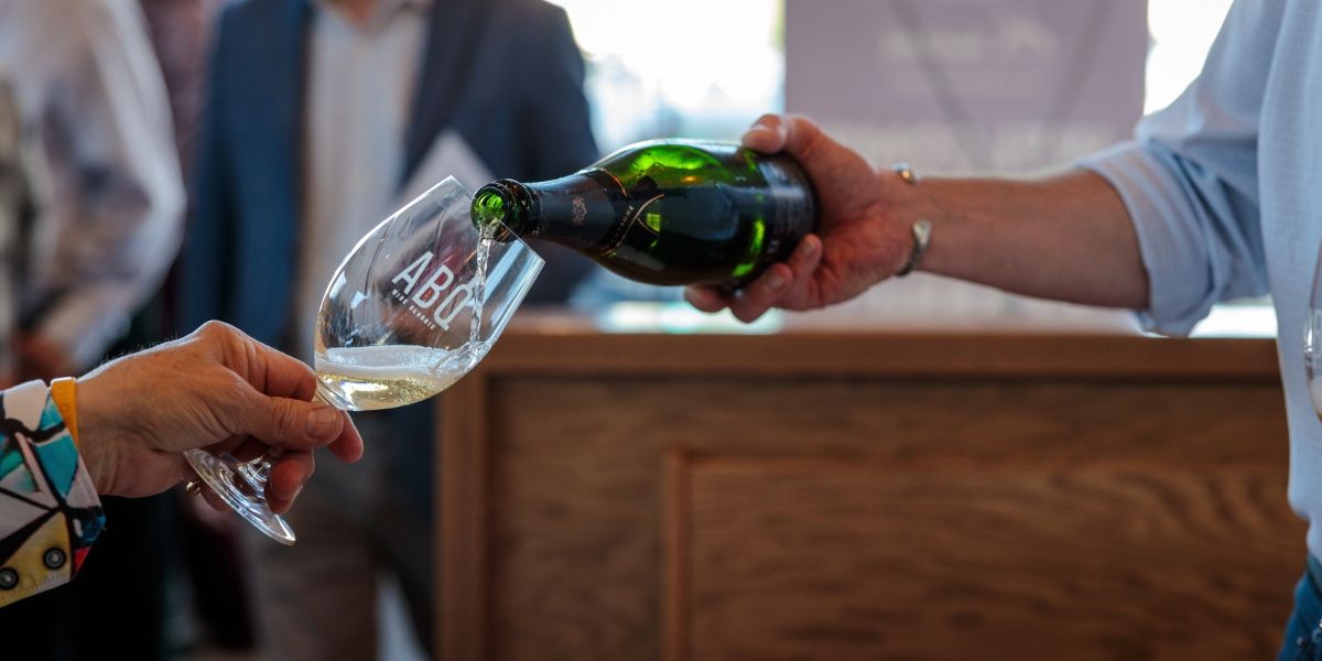 Photo by Andrew Holguin; an outstretched hand holds a wine glass being filled.